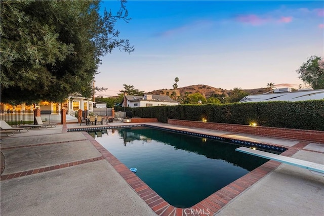 pool at dusk featuring a patio, a diving board, and a mountain view