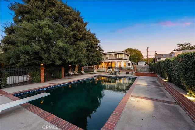 pool at dusk featuring a diving board and a patio