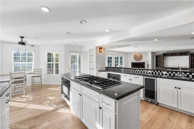 kitchen with sink, stainless steel gas cooktop, white cabinetry, beverage cooler, and oven