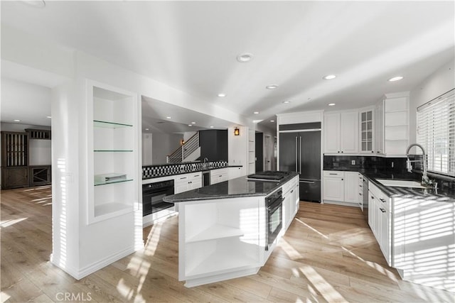 kitchen featuring a kitchen island, white cabinetry, sink, dark stone counters, and black appliances