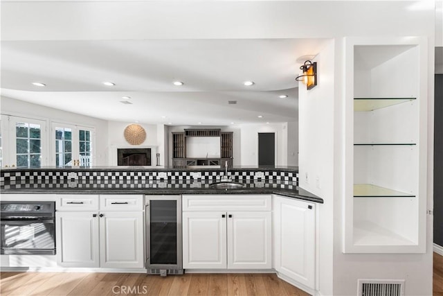 kitchen featuring black oven, sink, white cabinets, wine cooler, and backsplash