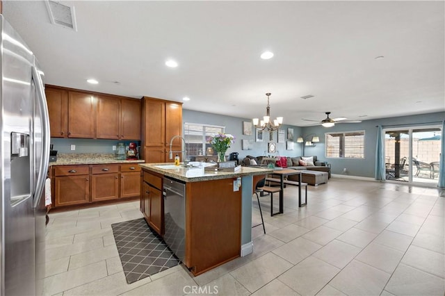 kitchen with sink, hanging light fixtures, an island with sink, stainless steel appliances, and light stone countertops