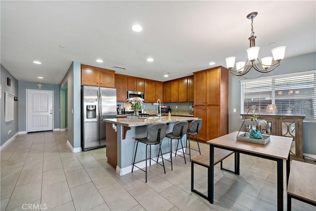 kitchen with light stone counters, a center island with sink, appliances with stainless steel finishes, a kitchen breakfast bar, and pendant lighting