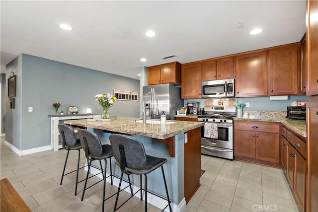 kitchen with sink, a kitchen breakfast bar, stainless steel appliances, light stone counters, and an island with sink