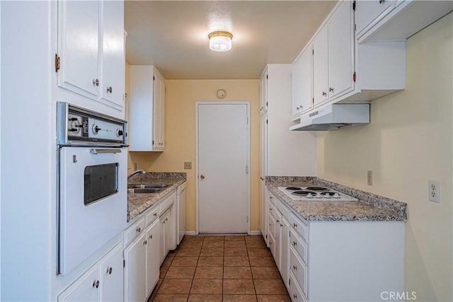 kitchen with dark tile patterned flooring, sink, white cabinetry, and white appliances