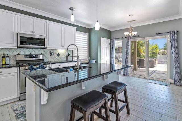 kitchen featuring white cabinetry, stainless steel appliances, an island with sink, sink, and backsplash