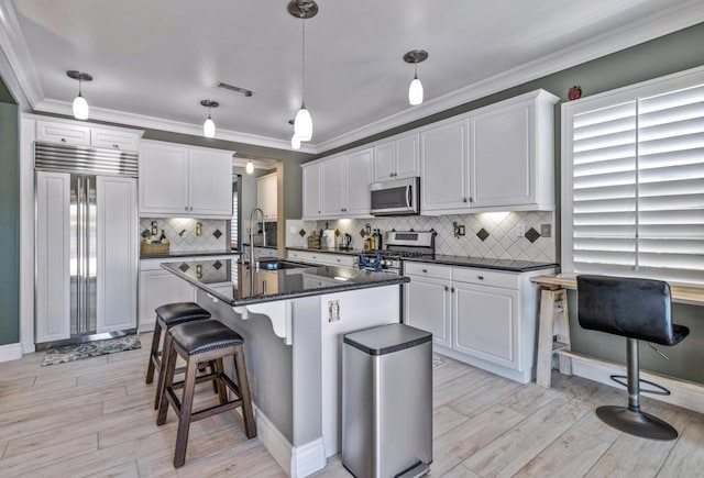 kitchen with appliances with stainless steel finishes, white cabinetry, sink, hanging light fixtures, and a kitchen island with sink