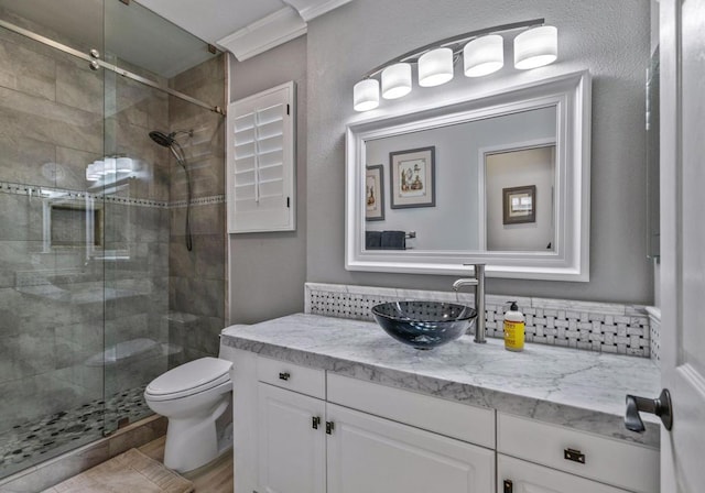 bathroom featuring an enclosed shower, vanity, toilet, and crown molding