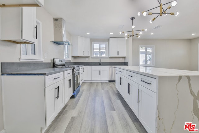 kitchen with hanging light fixtures, wall chimney exhaust hood, stainless steel appliances, and white cabinetry