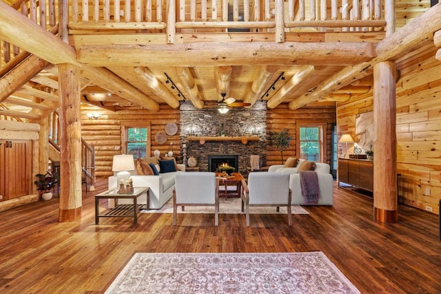 living room featuring rustic walls, dark hardwood / wood-style flooring, and a stone fireplace