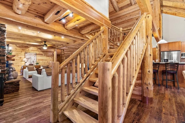 staircase featuring beamed ceiling, ceiling fan, rustic walls, hardwood / wood-style flooring, and wooden ceiling