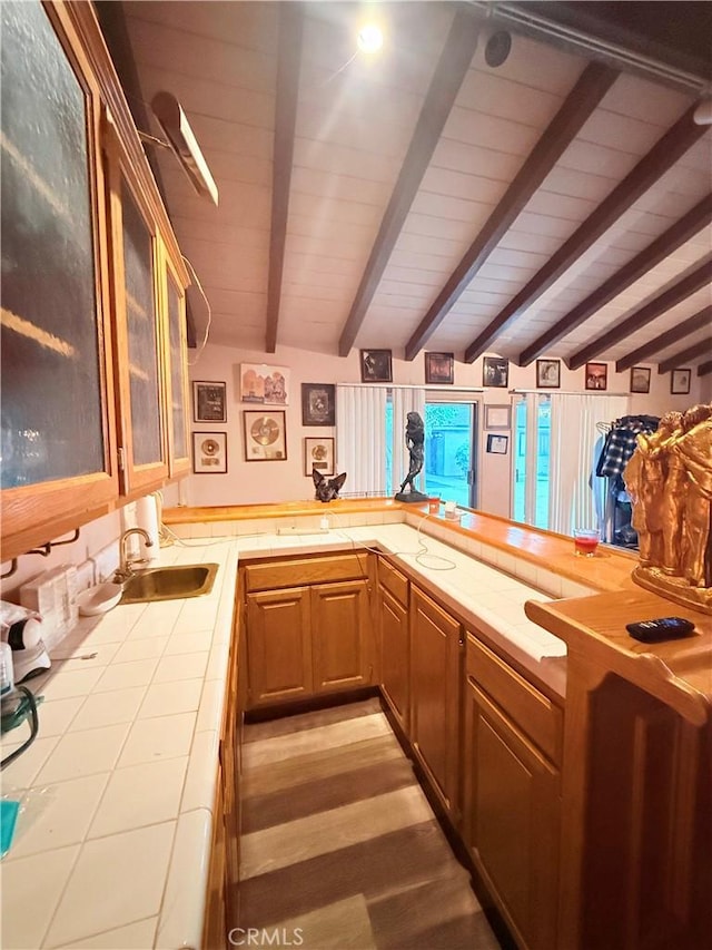 kitchen featuring tile counters, sink, and beamed ceiling