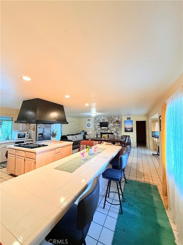 kitchen featuring tile counters, a fireplace, black gas cooktop, island range hood, and light tile patterned floors