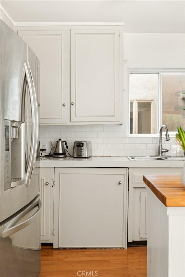 kitchen featuring light hardwood / wood-style floors, decorative backsplash, sink, white cabinets, and stainless steel fridge