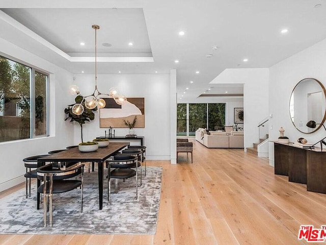 dining area with a notable chandelier, a tray ceiling, and light hardwood / wood-style flooring