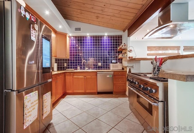 kitchen featuring lofted ceiling, wall chimney range hood, sink, stainless steel appliances, and light tile patterned flooring