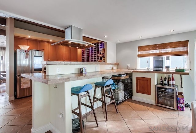 kitchen with island range hood, stainless steel fridge, a kitchen breakfast bar, light tile patterned floors, and kitchen peninsula