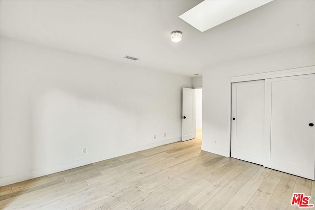 unfurnished bedroom with a closet, a skylight, and light hardwood / wood-style flooring