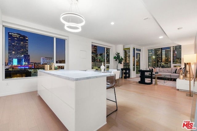 kitchen featuring light stone countertops, white cabinets, a kitchen bar, hanging light fixtures, and light hardwood / wood-style flooring