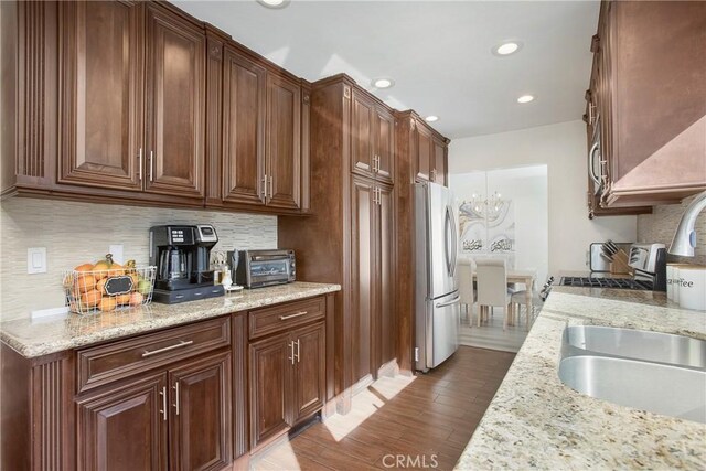 kitchen featuring light stone counters, light hardwood / wood-style flooring, an inviting chandelier, and stainless steel refrigerator