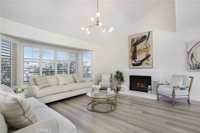 living room with plenty of natural light, a brick fireplace, a chandelier, and light hardwood / wood-style flooring