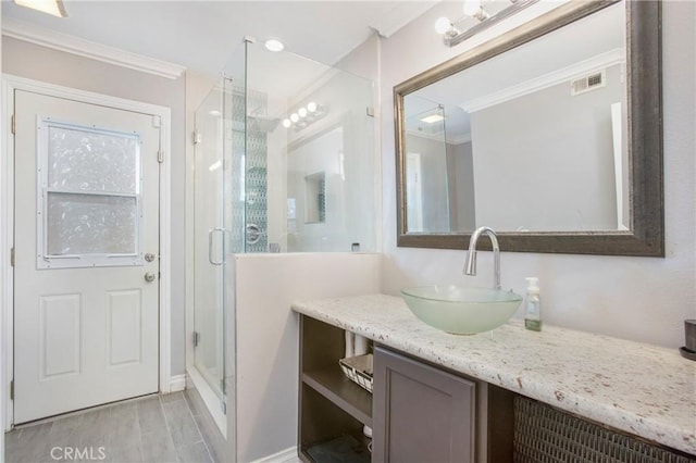 bathroom featuring a shower with shower door, vanity, and ornamental molding