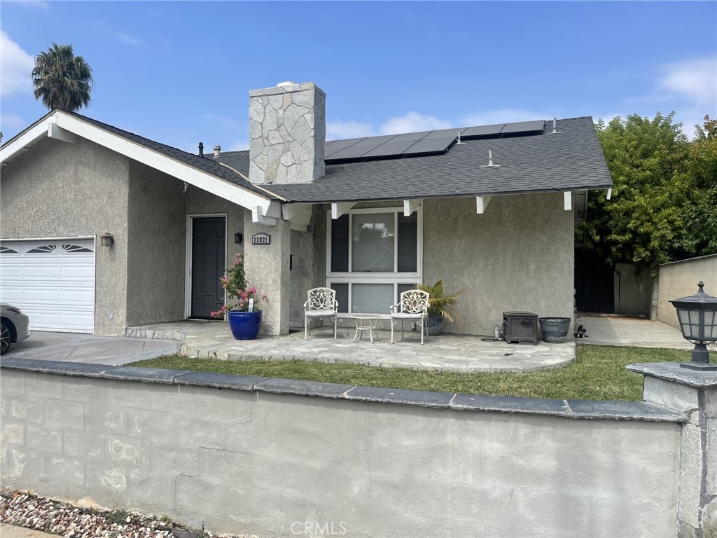 ranch-style home featuring a patio area, solar panels, and a garage