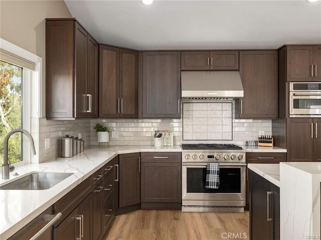 kitchen featuring sink, light wood-type flooring, stainless steel appliances, decorative backsplash, and wall chimney range hood