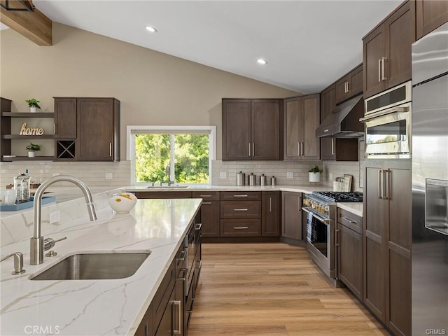 kitchen featuring sink, vaulted ceiling with beams, stainless steel appliances, light stone countertops, and wall chimney exhaust hood