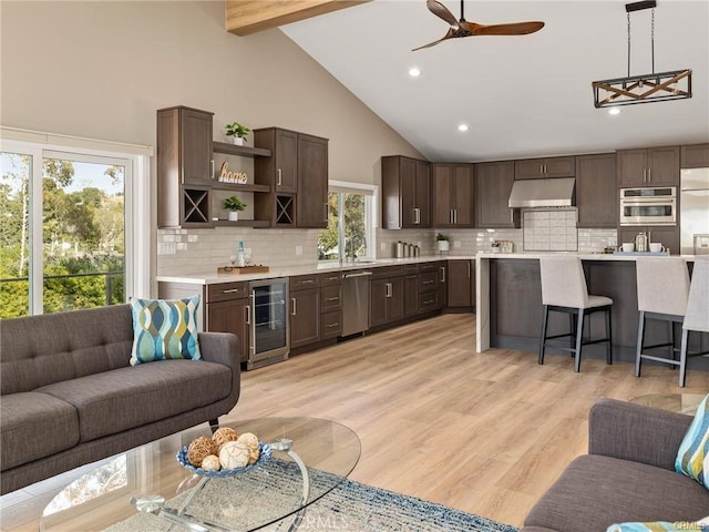 kitchen featuring a breakfast bar area, decorative light fixtures, high vaulted ceiling, stainless steel appliances, and beverage cooler