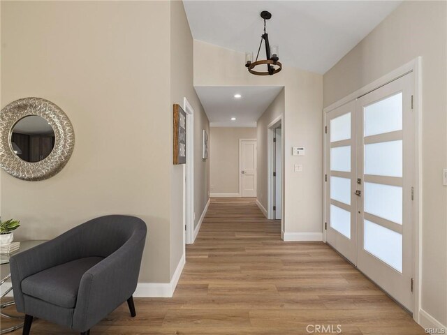 hall with vaulted ceiling, an inviting chandelier, light wood-type flooring, and french doors