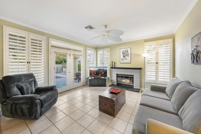 tiled living room featuring ceiling fan, french doors, a brick fireplace, and ornamental molding