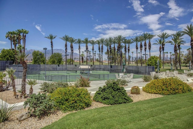 view of tennis court with a mountain view, a yard, and a patio