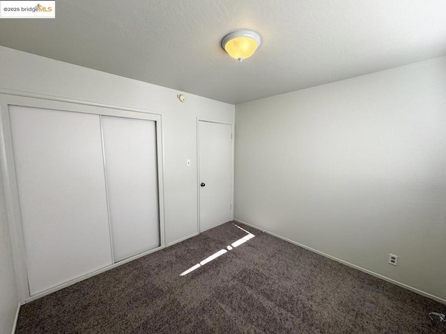 unfurnished bedroom with a closet and dark colored carpet