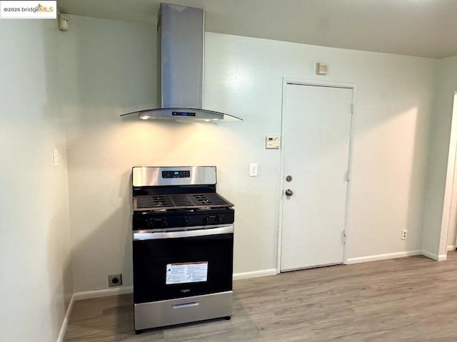 kitchen with light hardwood / wood-style floors, wall chimney range hood, and stainless steel gas range