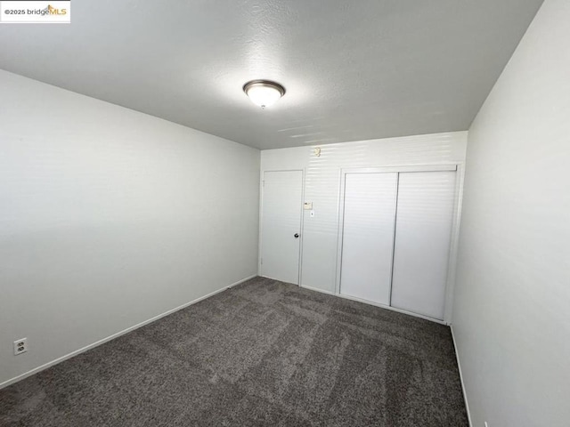 unfurnished bedroom with a textured ceiling, a closet, and dark carpet