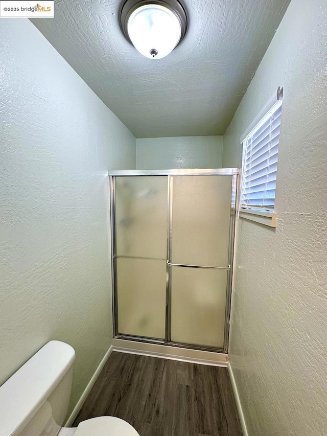 bathroom with wood-type flooring, toilet, and a shower with door