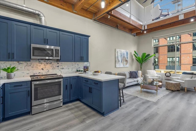 kitchen featuring wooden ceiling, kitchen peninsula, a towering ceiling, stainless steel appliances, and decorative backsplash