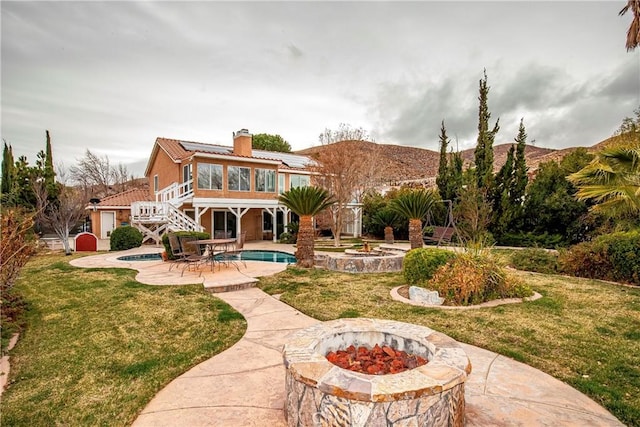 rear view of house with a sunroom, a yard, a patio area, and an outdoor fire pit