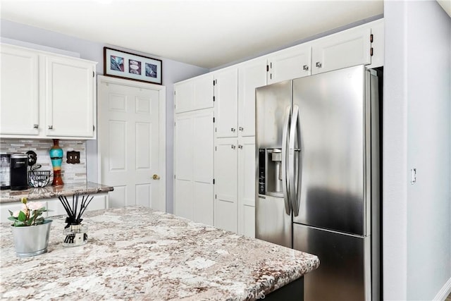 kitchen featuring light stone countertops, stainless steel fridge with ice dispenser, decorative backsplash, and white cabinets