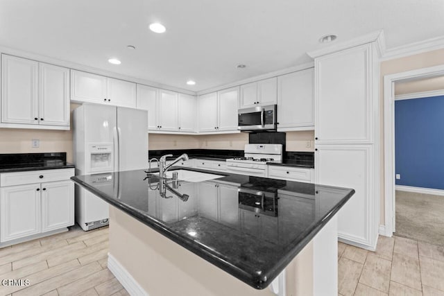 kitchen featuring white appliances, dark stone countertops, a kitchen island with sink, and white cabinets