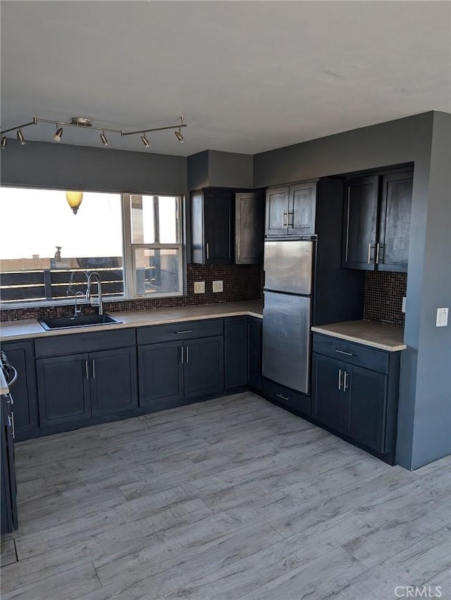 kitchen featuring decorative backsplash, sink, light hardwood / wood-style floors, and stainless steel refrigerator