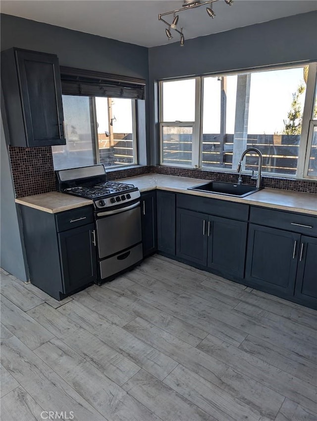 kitchen with decorative backsplash, stainless steel gas stove, sink, and light hardwood / wood-style flooring