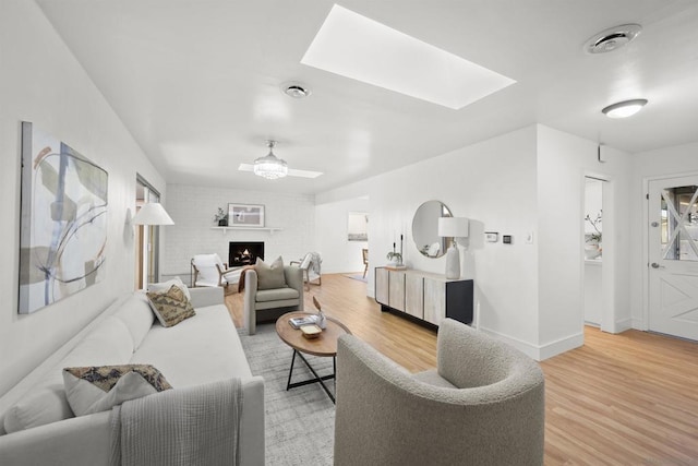 living room with ceiling fan, a skylight, and wood-type flooring