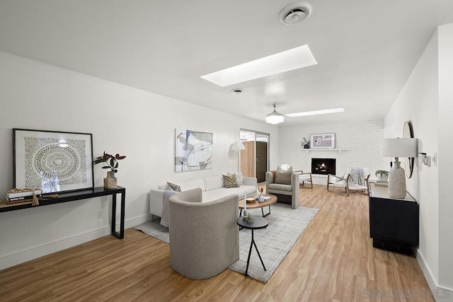 living room with a brick fireplace, a skylight, and wood-type flooring