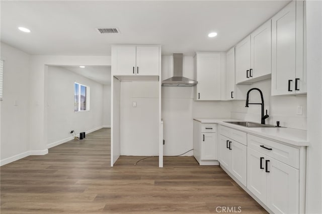 kitchen with hardwood / wood-style flooring, wall chimney exhaust hood, white cabinets, and sink