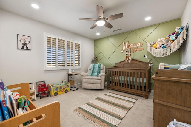 carpeted bedroom with ceiling fan and a nursery area