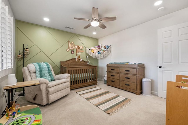 bedroom with ceiling fan, a nursery area, and light carpet