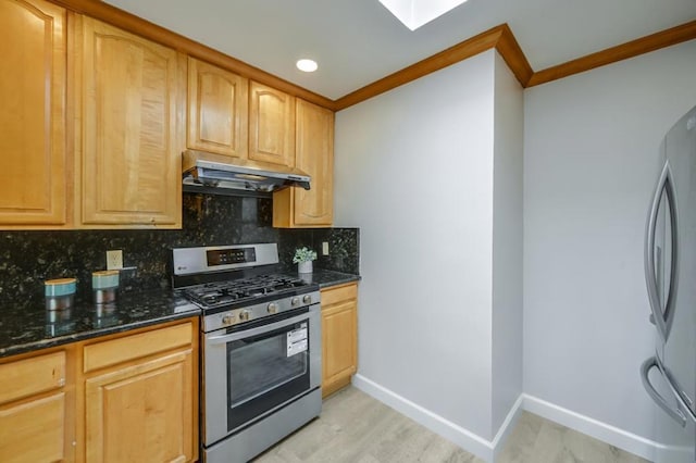 kitchen featuring appliances with stainless steel finishes, dark stone countertops, decorative backsplash, ornamental molding, and light hardwood / wood-style flooring