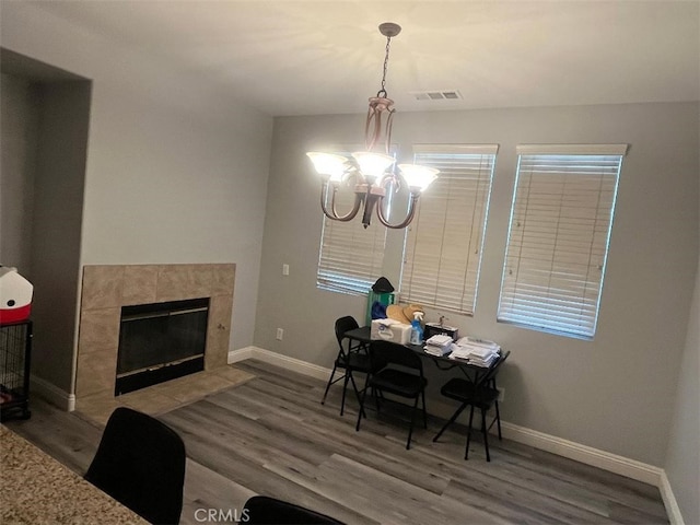 dining area featuring a tile fireplace, an inviting chandelier, and hardwood / wood-style floors